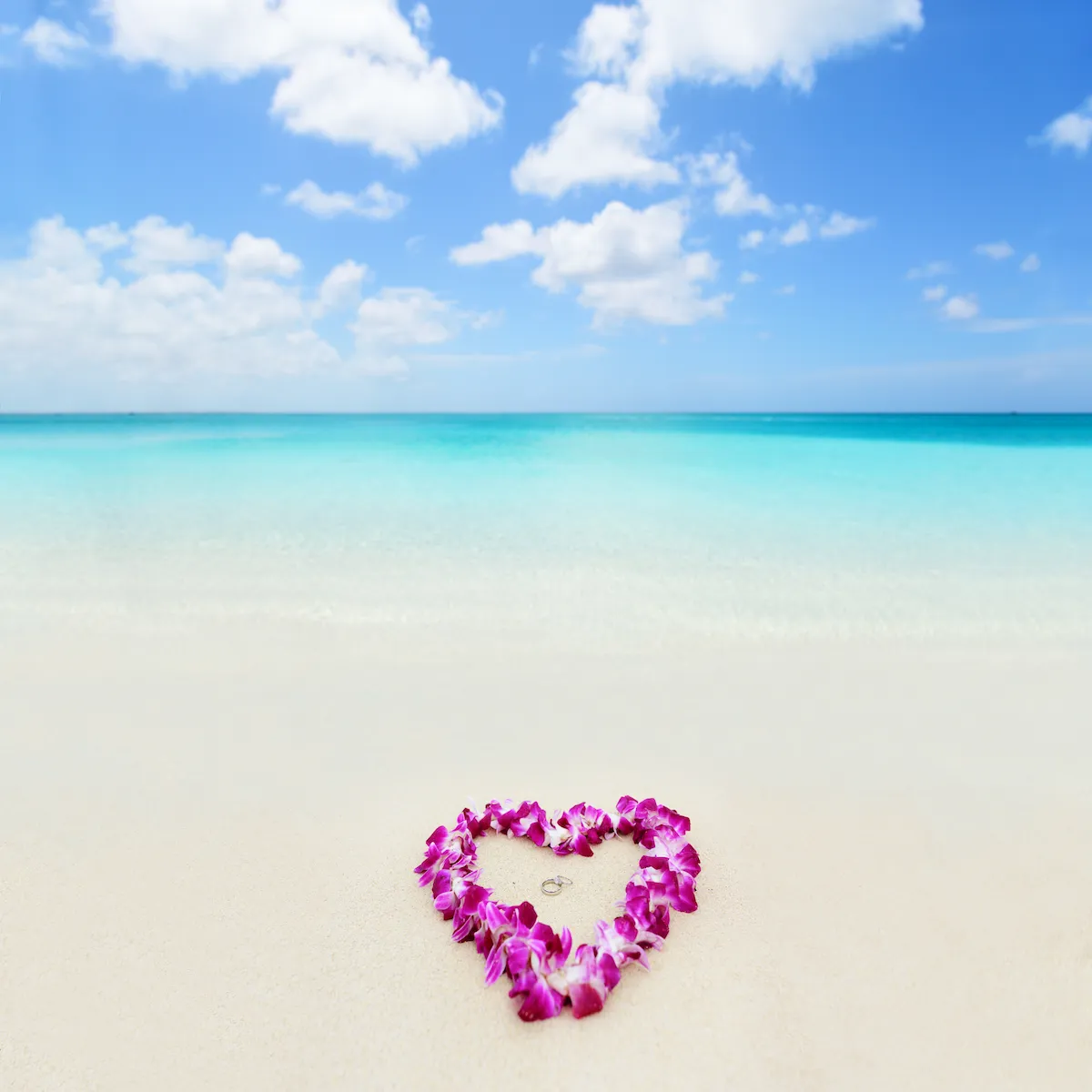 A heart-shaped floral lei on a Maui beach with wedding rings at its center