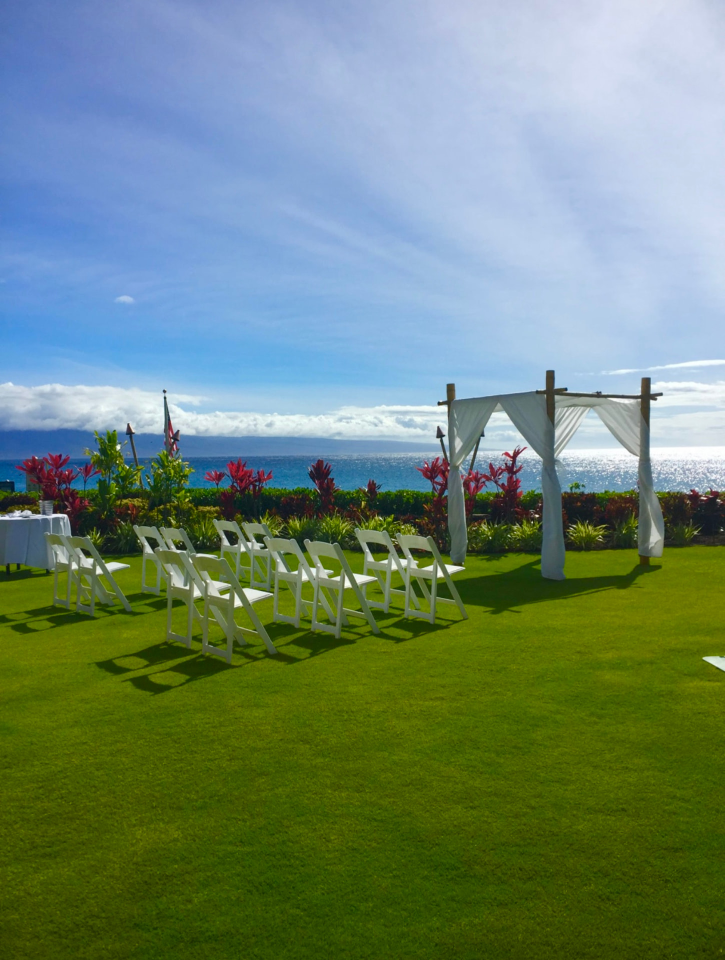 An oceanfront Maui wedding ceremony with white chairs, a draped arch, tropical flowers, and the Pacific in the background