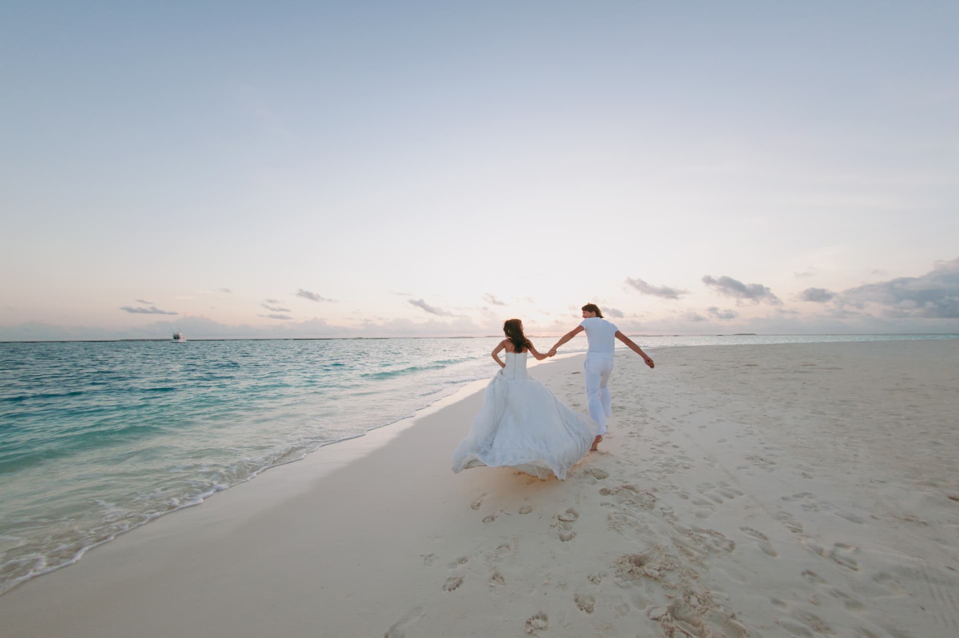 Bride and groom running hand in hand along a white sand beach at sunset in Maui