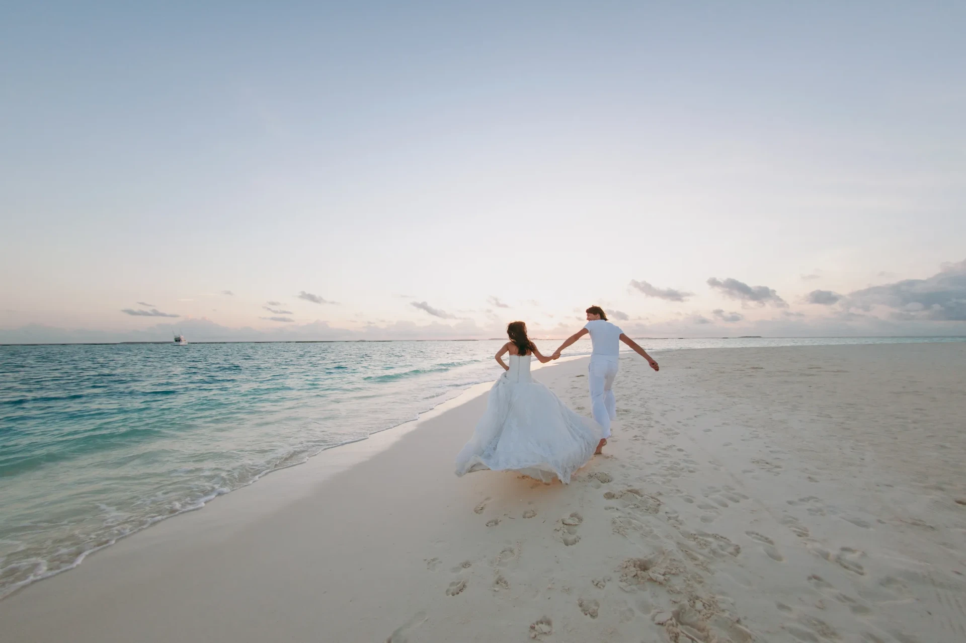Bride and groom running hand in hand along a white sand beach at sunset in Maui